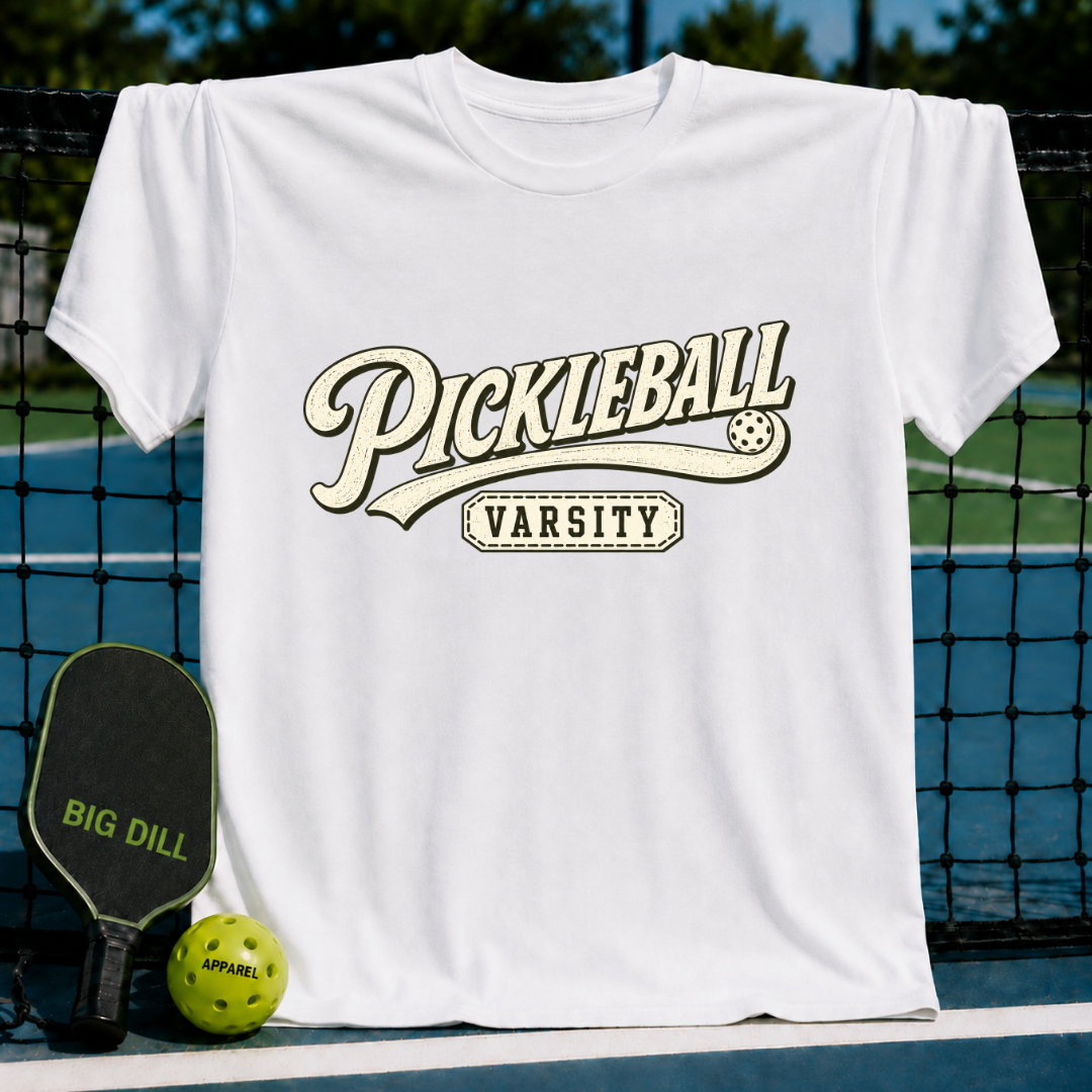 White crew neck t-shirt featuring a vintage-style Pickleball Varsity graphic, displayed on a pickleball court net.
