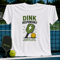 White unisex t-shirt featuring a green pickleball paddle graphic with a lightning bolt and the text Dink Responsibly.