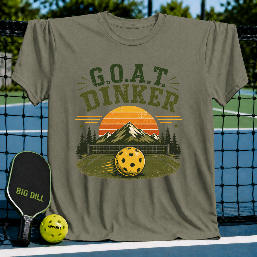 Olive green unisex t-shirt featuring a retro pickleball sunset landscape graphic with G.O.A.T. DINKER text on a court background.