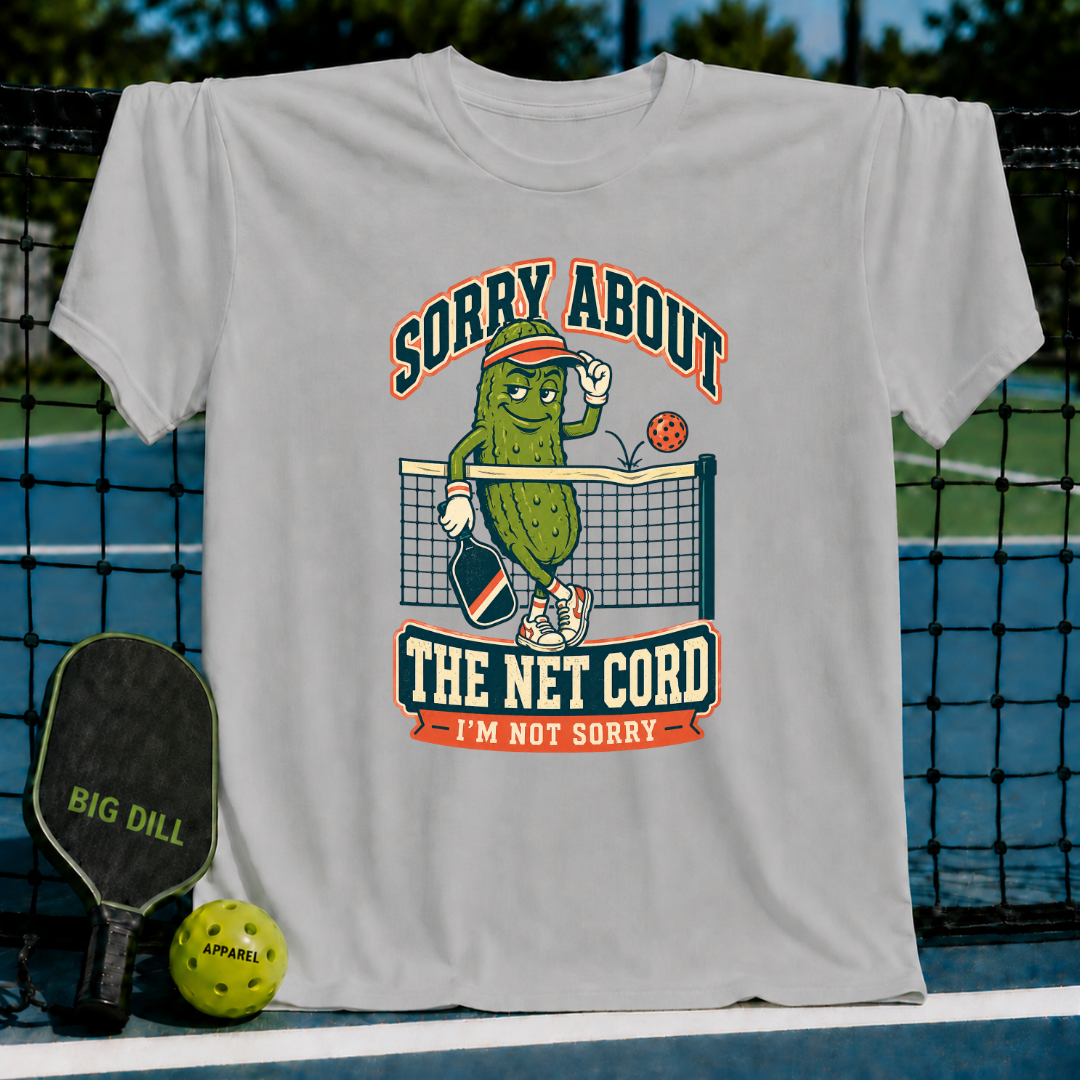 Light grey t-shirt featuring a cartoon pickle playing pickleball with the text Sorry About The Net Cord I'm Not Sorry.