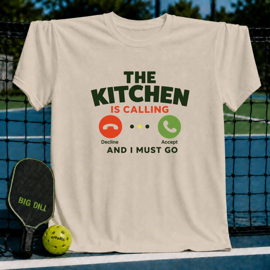 Cream-colored unisex t-shirt featuring a phone call UI graphic with The Kitchen Is Calling text on a pickleball court.