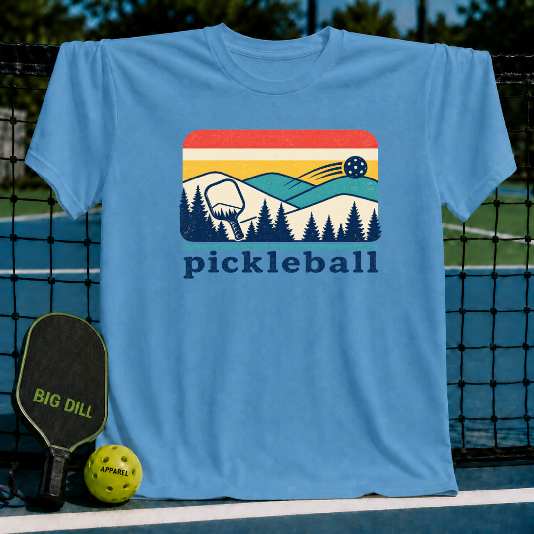Light blue unisex t-shirt featuring a retro mountain, pine tree, and pickleball graphic with the word pickleball printed below.