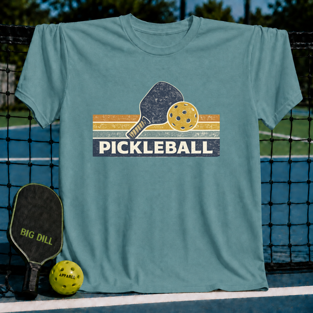 Vintage blue t-shirt featuring a retro pickleball paddle and ball graphic with striped accents on a court background.