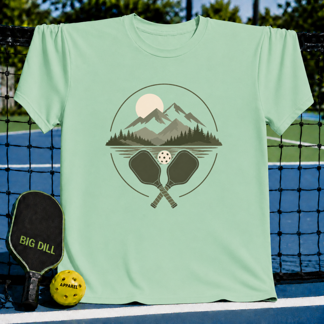 Mint green crewneck T-shirt featuring a circular graphic of mountains, a forest, and crossed pickleball paddles.