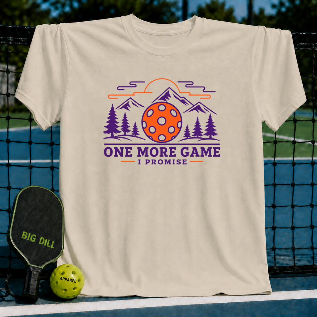 Beige cotton t-shirt featuring a colorful pickleball, mountain, and forest graphic with the text One More Game I Promise.