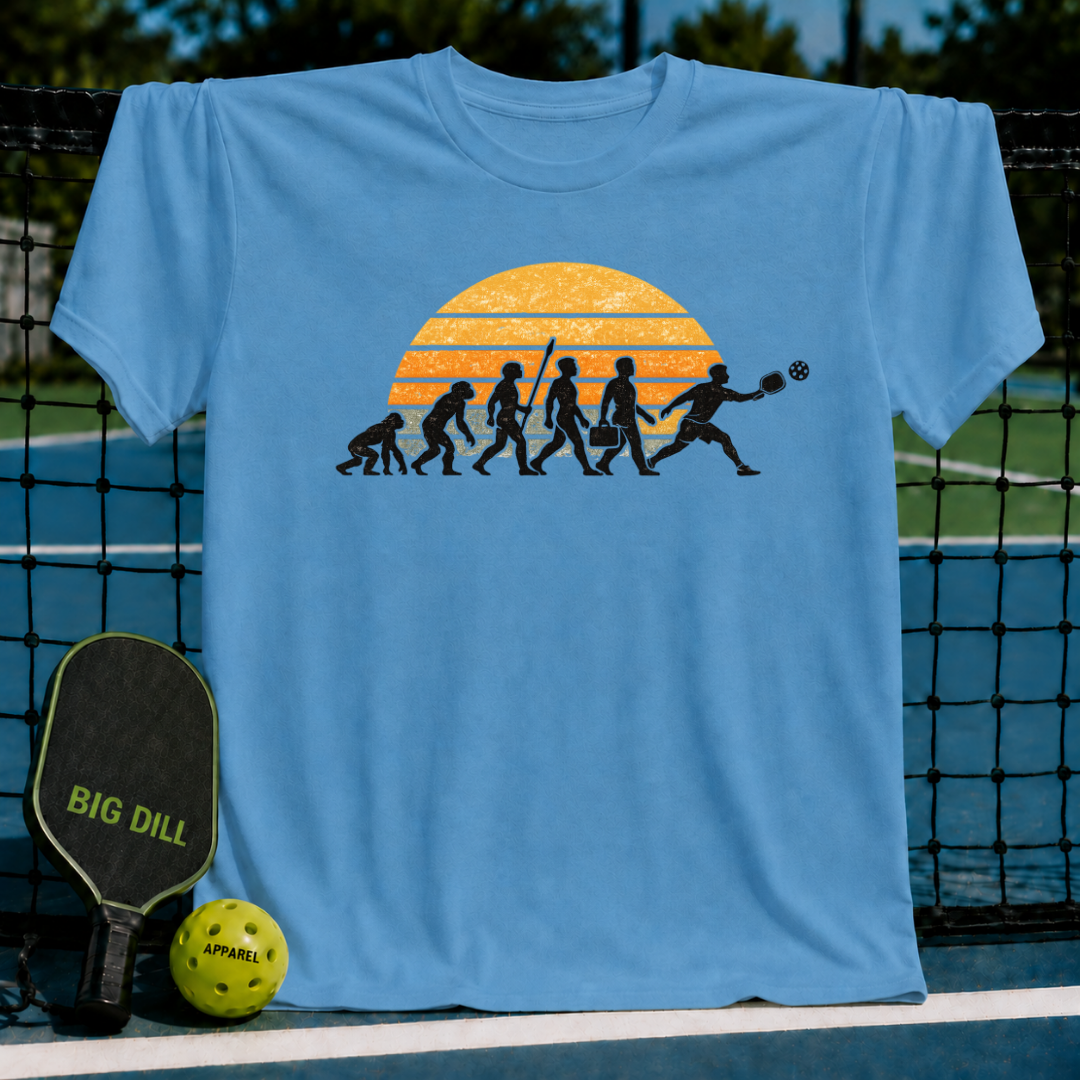Light blue unisex t-shirt featuring a retro sunset and human evolution graphic with a pickleball player on a court.