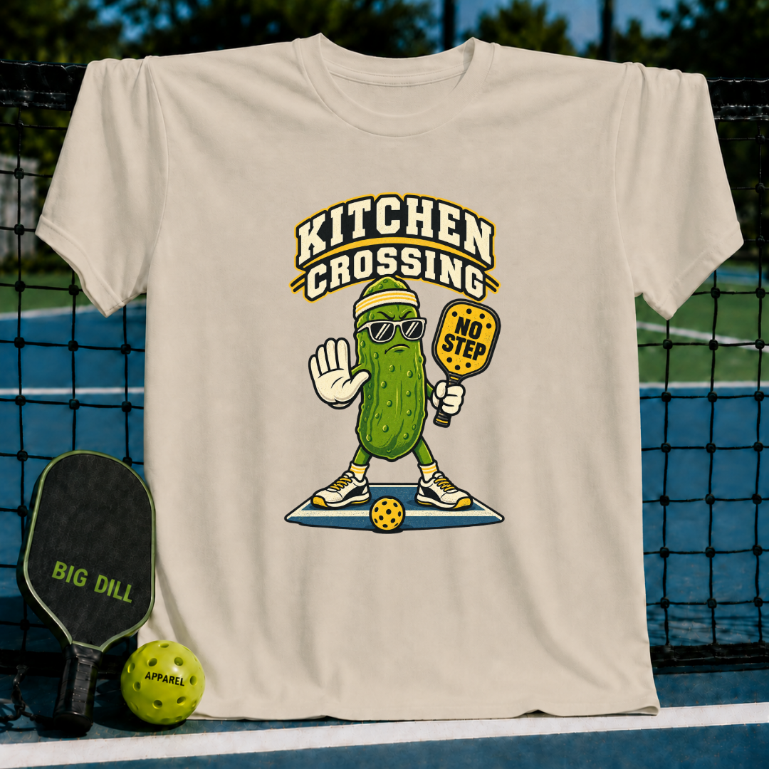 Beige crewneck t-shirt featuring a cartoon pickle wearing sunglasses and holding a pickleball paddle on a court.
