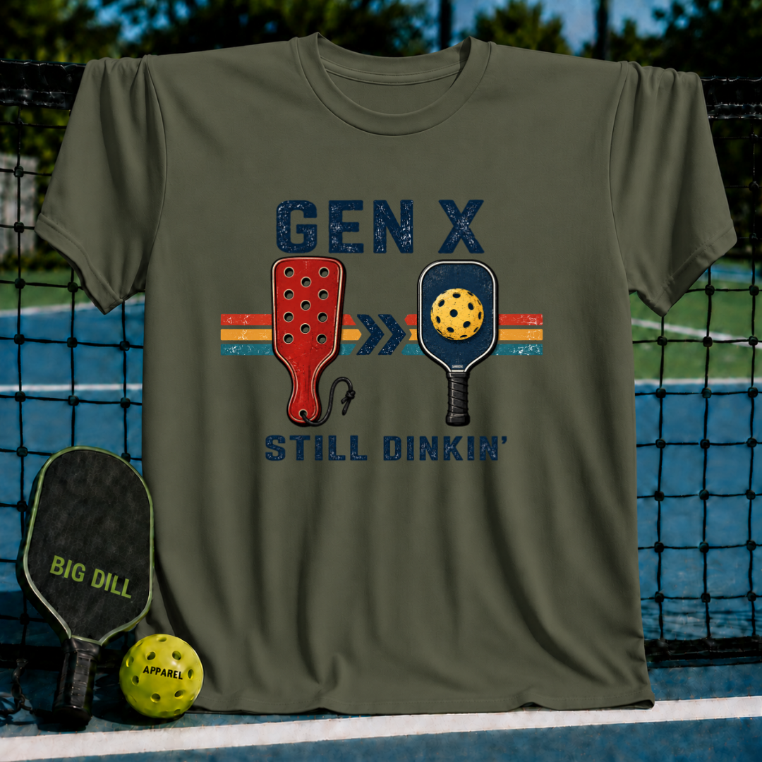 Olive green unisex t-shirt with a retro Gen X Still Dinkin' pickleball graphic, displayed on a pickleball court net.