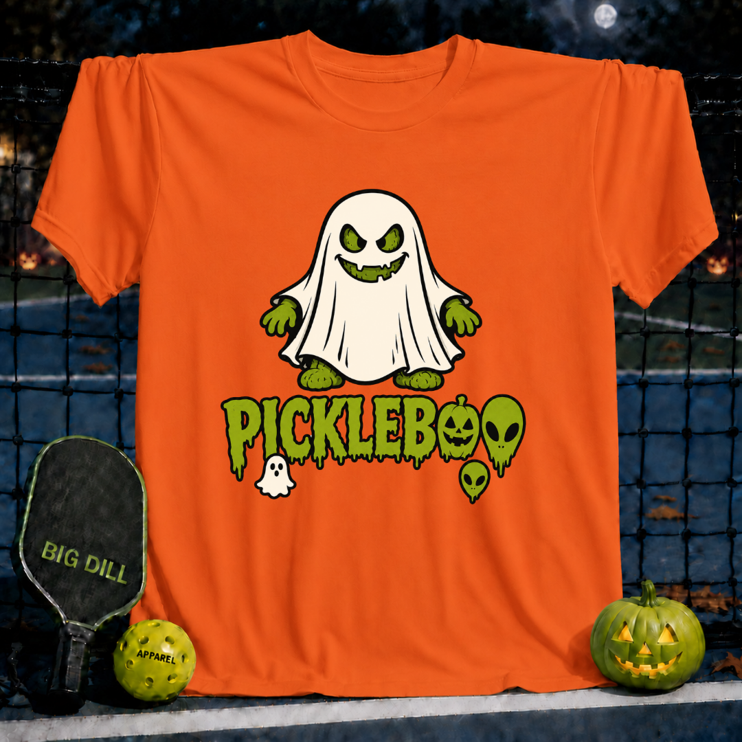 Bright orange unisex t-shirt featuring a spooky ghost pickle graphic and PickleBoo text, displayed on a pickleball court.