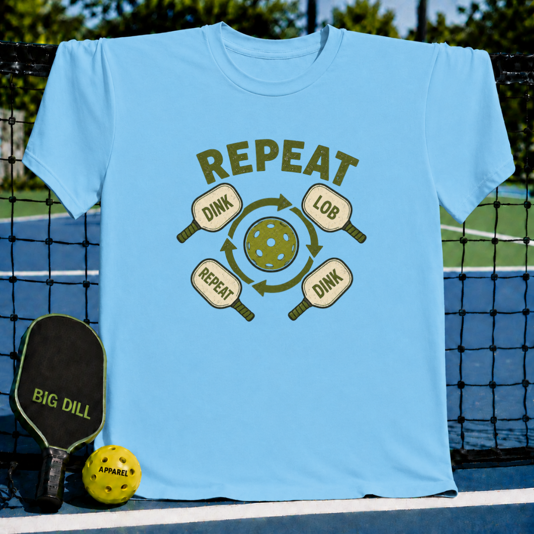 Light blue crew neck t-shirt featuring a green pickleball graphic with dink, lob, and repeat text on a pickleball court.