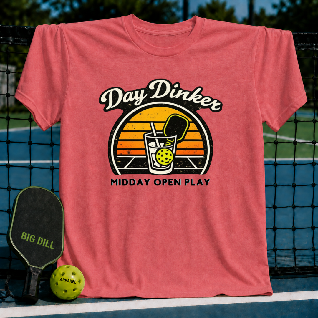 Coral pink unisex t-shirt featuring a retro sunset graphic of a pickleball paddle and ball in a glass on a court.