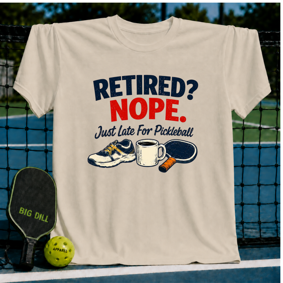 Beige crewneck T-shirt featuring a Retired? Nope. Just Late For Pickleball graphic with a sneaker, coffee mug, and paddle.