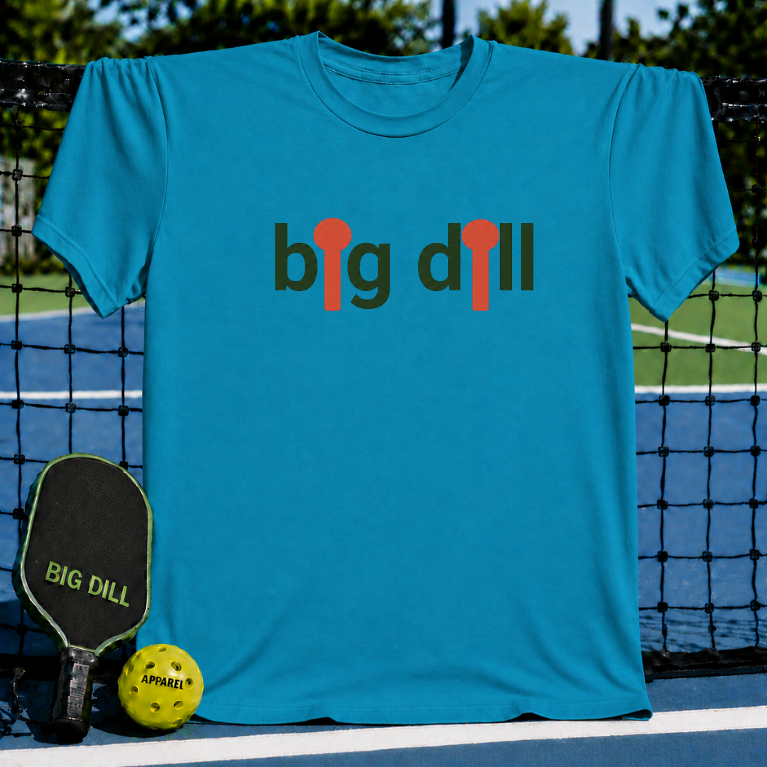 Blue unisex t-shirt featuring a Big Dill graphic with orange pickleball paddle icons, displayed on a pickleball court.