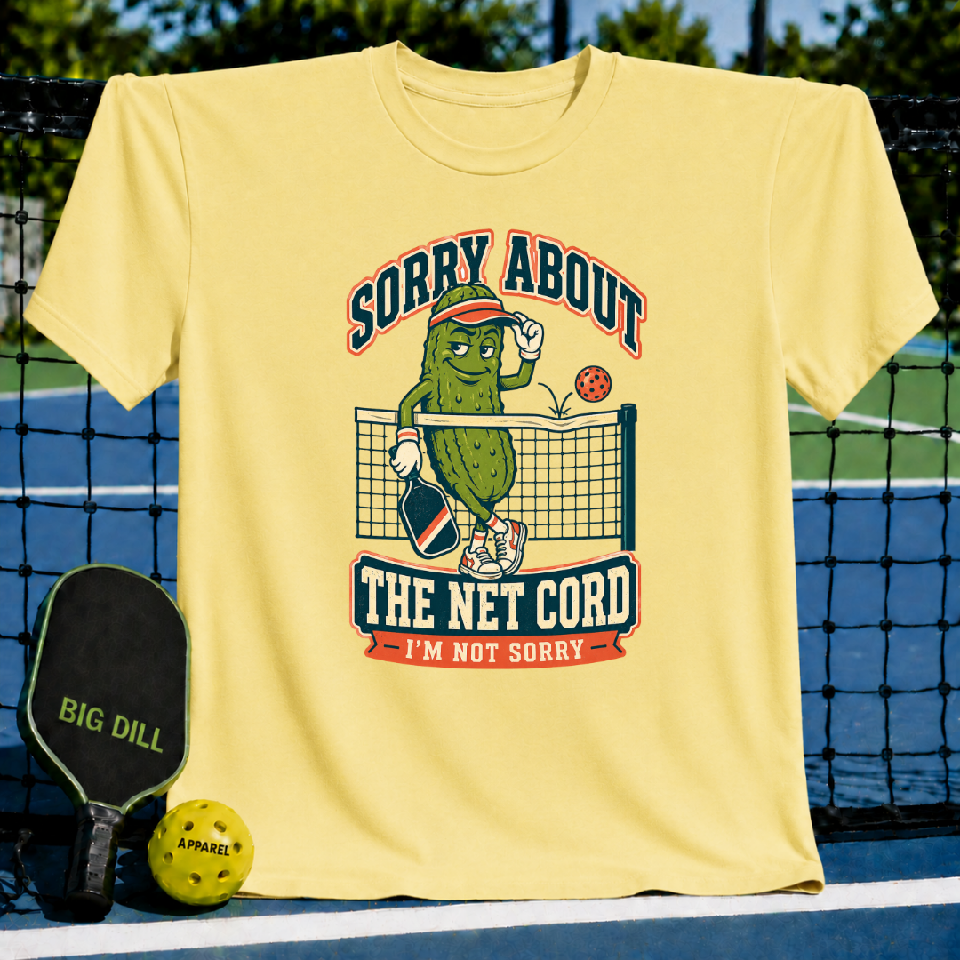 Light yellow crew neck t-shirt featuring a cartoon pickle playing pickleball with the text Sorry About The Net Cord.