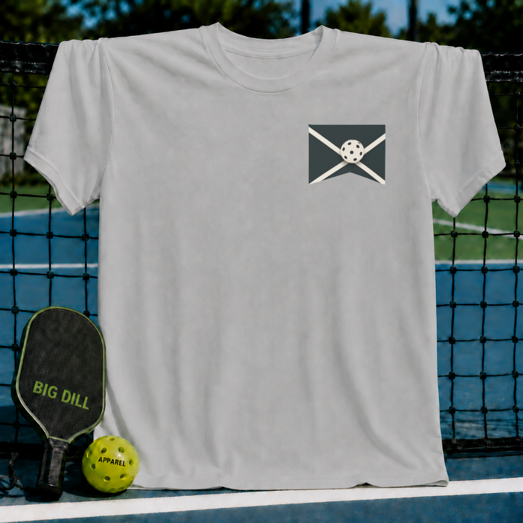 Light grey unisex On The Edge t-shirt featuring a small pickleball graphic on the chest, displayed on a pickleball court.