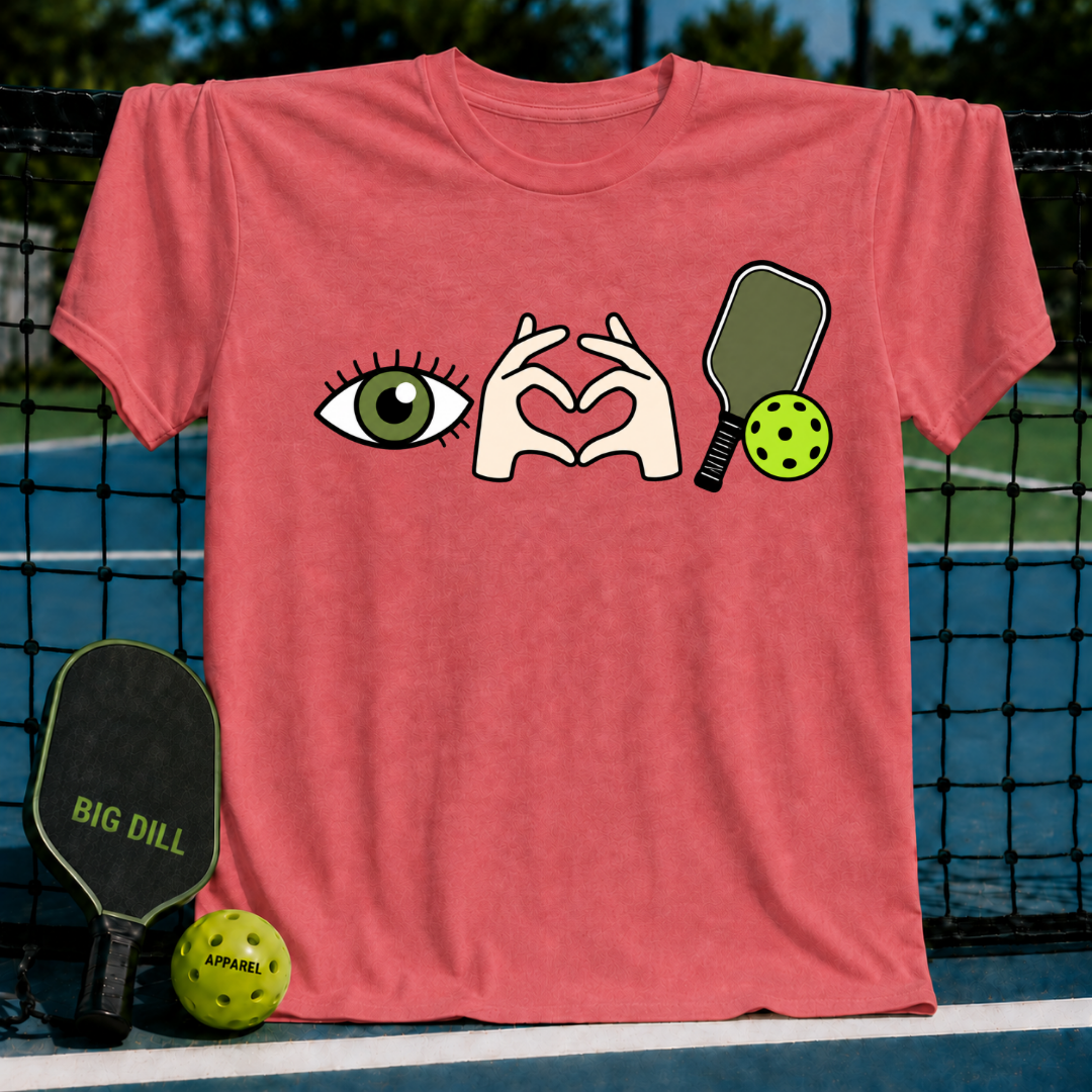 Coral pink cotton t-shirt featuring an eye, heart-shaped hands, and pickleball paddle graphic on a court background.
