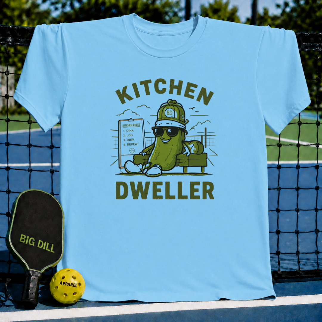 Light blue crew neck t-shirt featuring a pickleball-themed graphic of a cool pickle character with sunglasses and a clipboard.