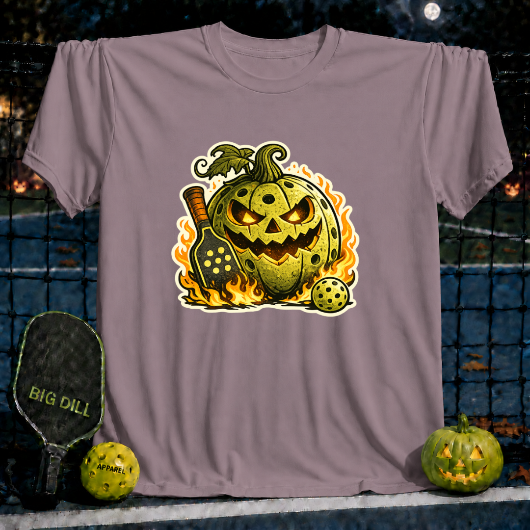 Sand-colored unisex t-shirt featuring a flaming jack-o'-lantern pickleball graphic with a paddle and ball.