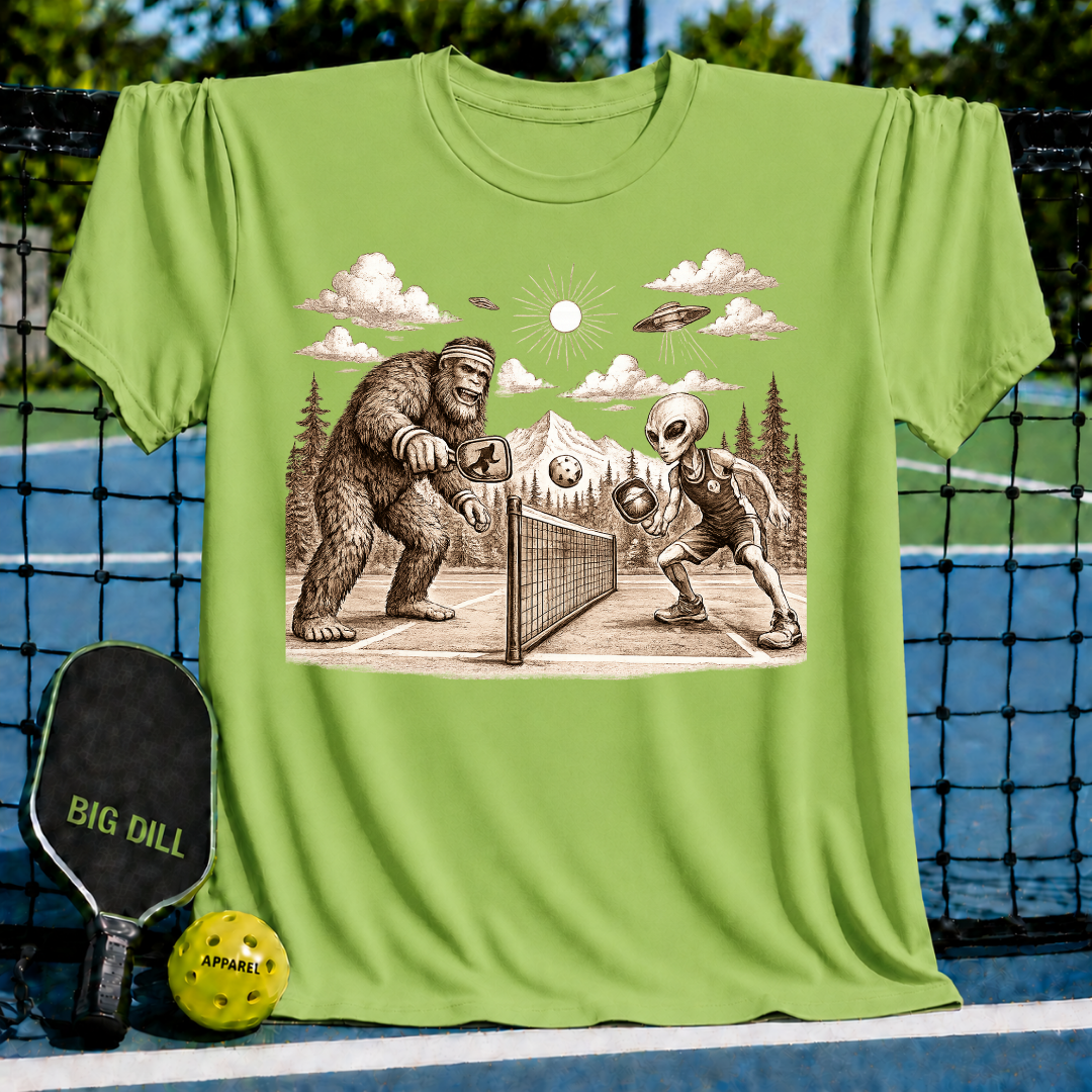 Light green unisex t-shirt featuring a vintage-style graphic of Bigfoot and an alien playing pickleball on a court.