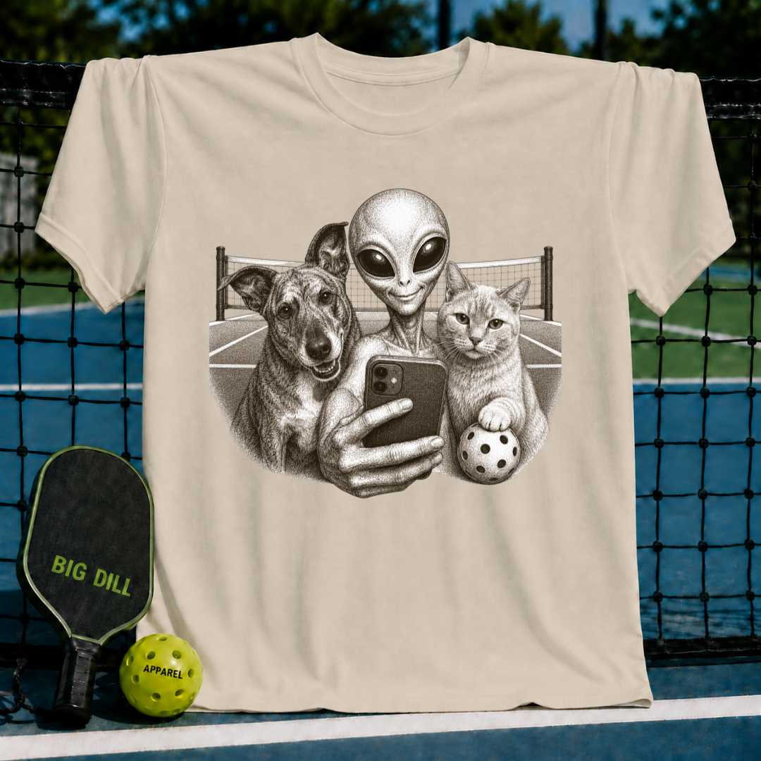 Light beige unisex t-shirt featuring a vintage-style illustration of an alien, dog, and cat taking a pickleball court selfie.