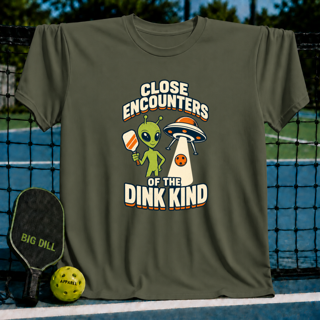 Olive green crewneck t-shirt featuring a cartoon alien holding a pickleball paddle next to a UFO and text graphic.