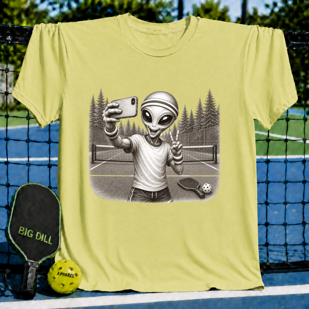 Sage green unisex t-shirt featuring a vintage-style illustration of an alien taking a selfie on a pickleball court.