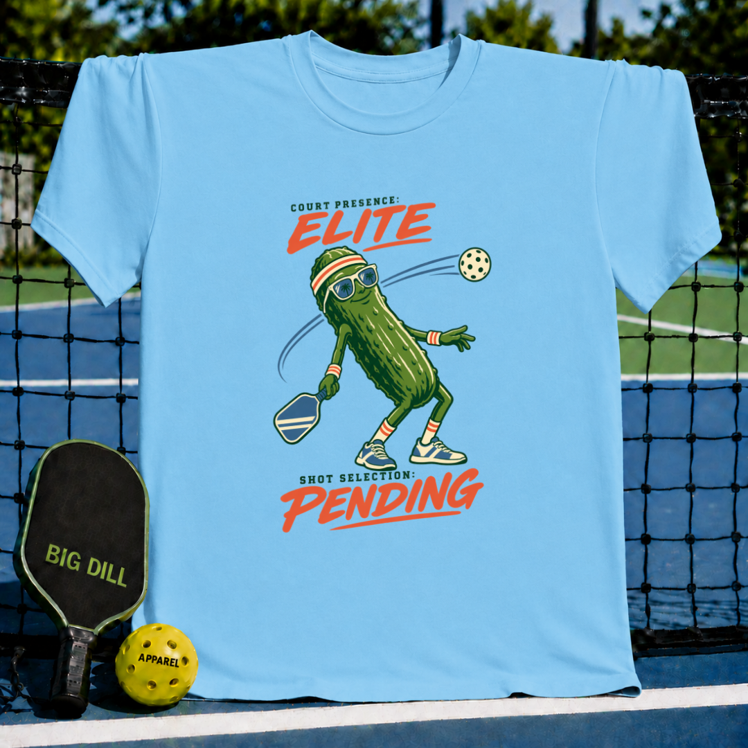 Light blue crewneck T-shirt featuring a cartoon pickle playing pickleball with sunglasses and text graphic.