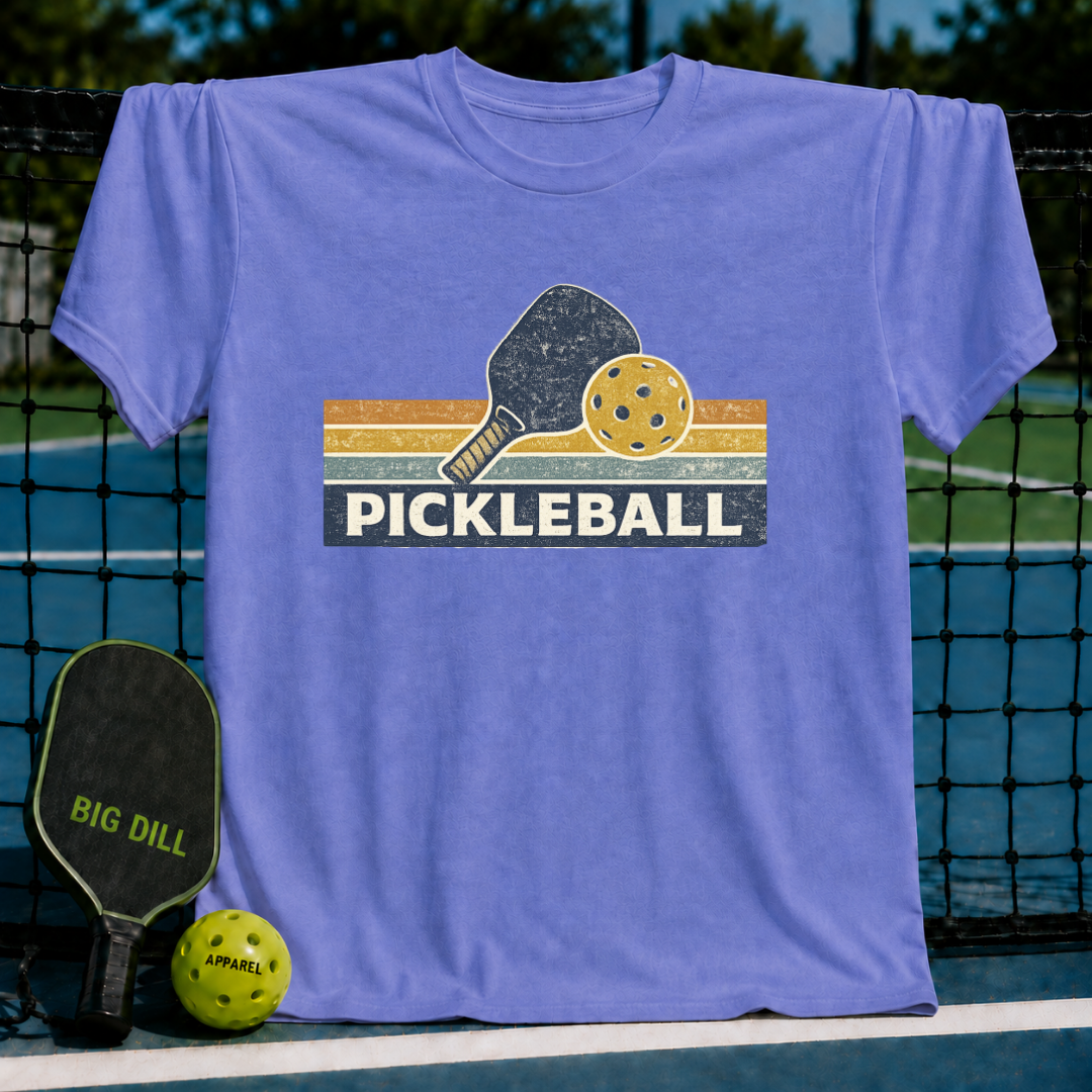 Periwinkle vintage-style cotton t-shirt featuring a retro pickleball paddle and ball graphic on a court background.