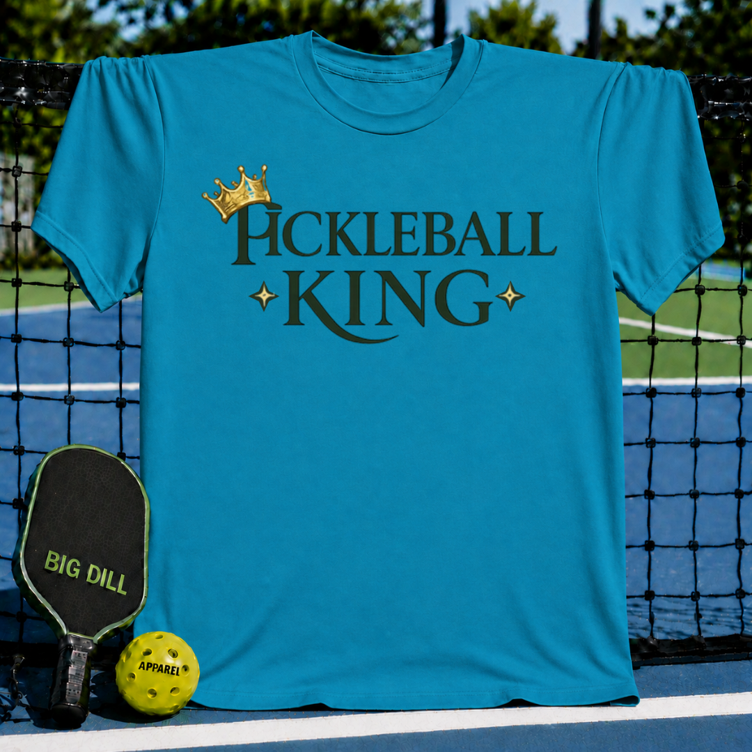 Bright blue unisex t-shirt featuring a gold crown and dark Pickleball King text, displayed on a pickleball court.