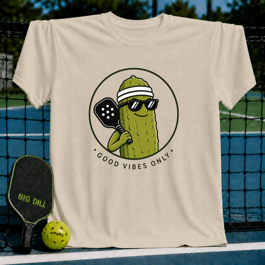 Cream-colored unisex t-shirt featuring a smiling pickle character in sunglasses and a visor with a pickleball paddle.