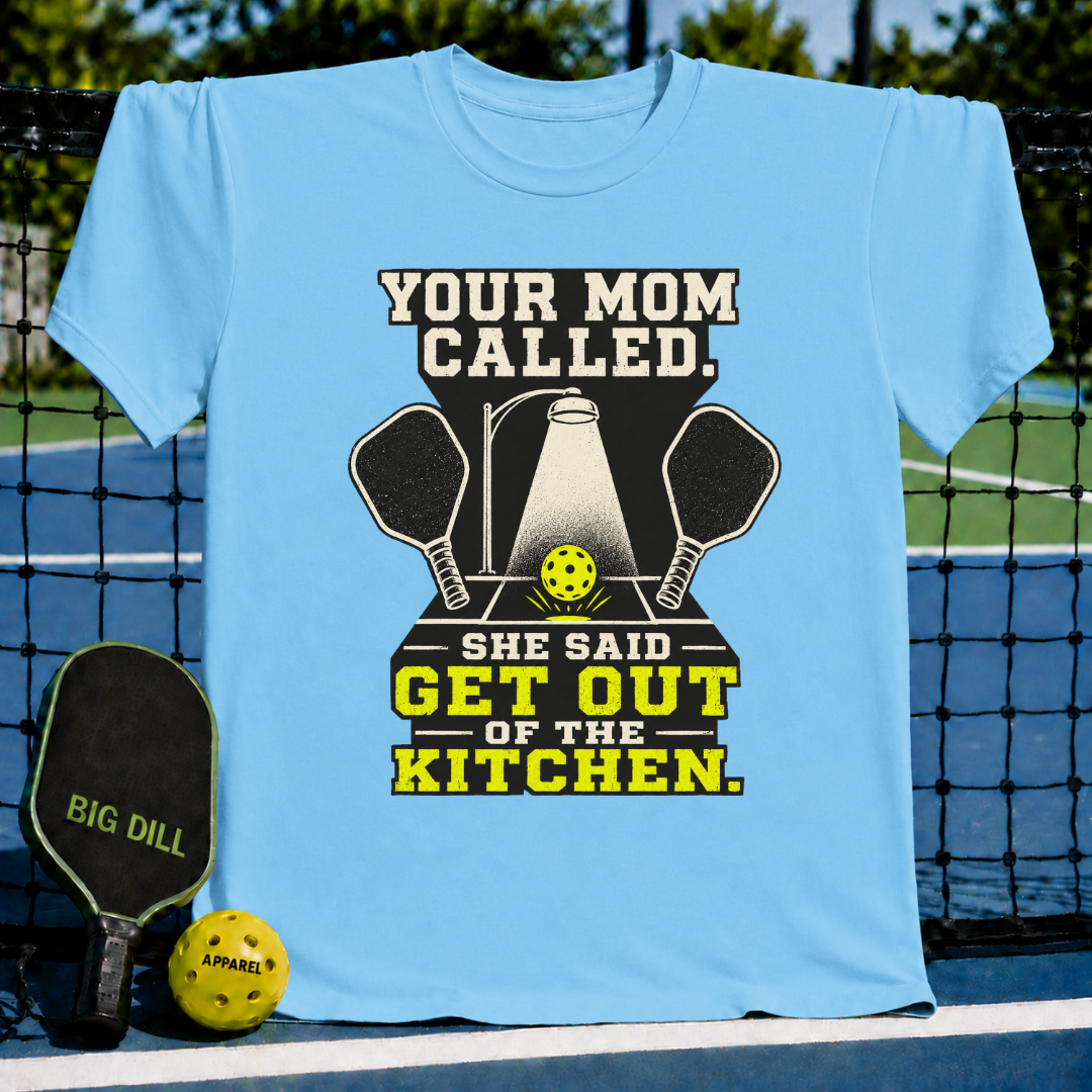 Light blue unisex t-shirt featuring a pickleball graphic with two paddles, a spotlight, and the text Your Mom Called Get Out Of The Kitchen.
