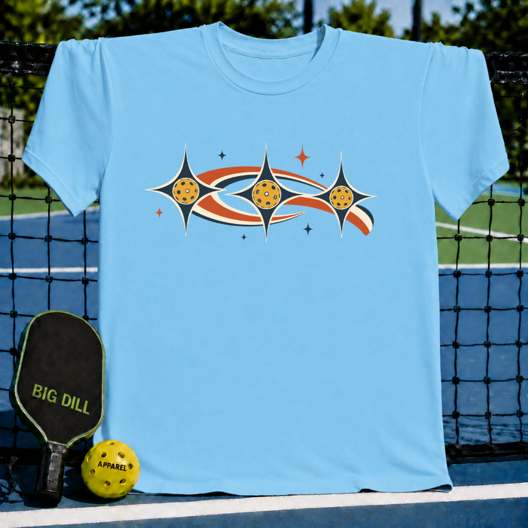 Light blue unisex t-shirt featuring a retro celestial pickleball graphic with stars and orbits on a pickleball court.