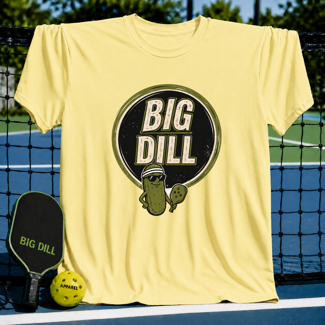 Light yellow crew neck t-shirt featuring a Big Dill pickle graphic with a pickleball paddle on a court background.