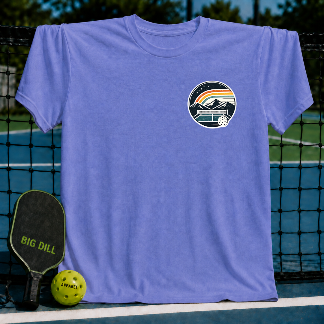 Periwinkle blue unisex t-shirt featuring a circular mountain and pickleball court graphic on a pickleball court background.
