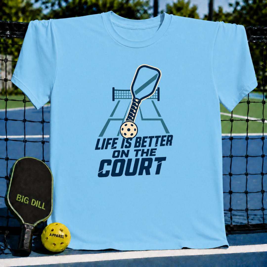 Light blue crew neck t-shirt featuring a pickleball court graphic with a paddle and ball and the text Life is Better on the Court.