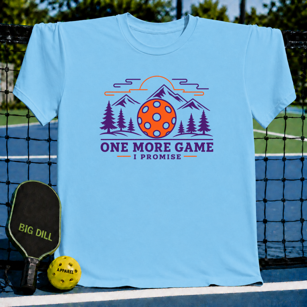 Light blue crew neck t-shirt featuring a mountain, pine tree, and pickleball graphic with the text One More Game I Promise.