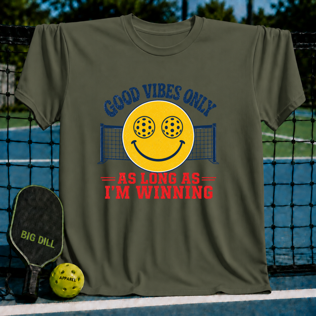 Olive green unisex t-shirt featuring a retro smiley face with pickleball eyes and the text Good Vibes Only As Long As I'm Winning.