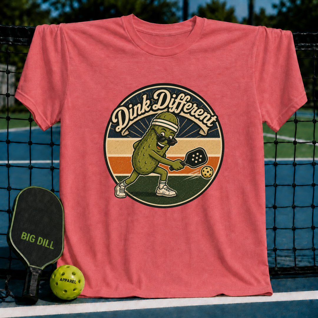 Coral unisex t-shirt featuring a retro pickleball graphic of a pickle in a visor hitting a ball, displayed on a court net.