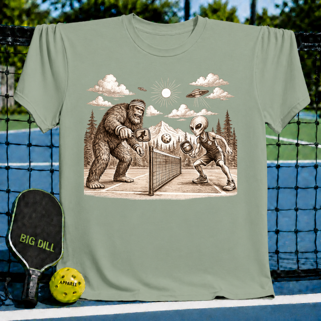 Sage green unisex t-shirt featuring a vintage-style graphic of Bigfoot and an alien playing pickleball on a court.