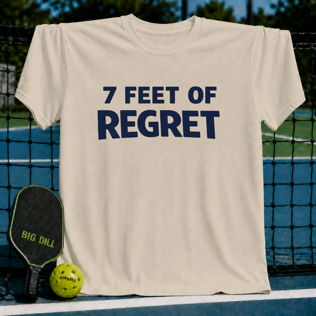 Beige unisex t-shirt featuring navy block text reading 7 Feet Of Regret, displayed on a pickleball court with a paddle and ball.
