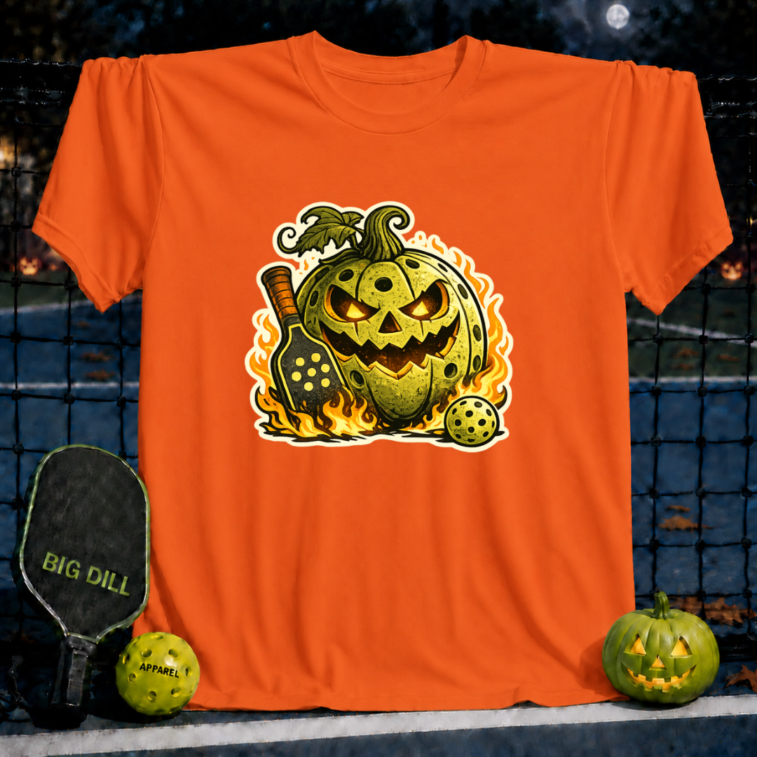 Orange unisex t-shirt featuring a flaming jack-o'-lantern pickleball graphic with a paddle and ball on a court background.