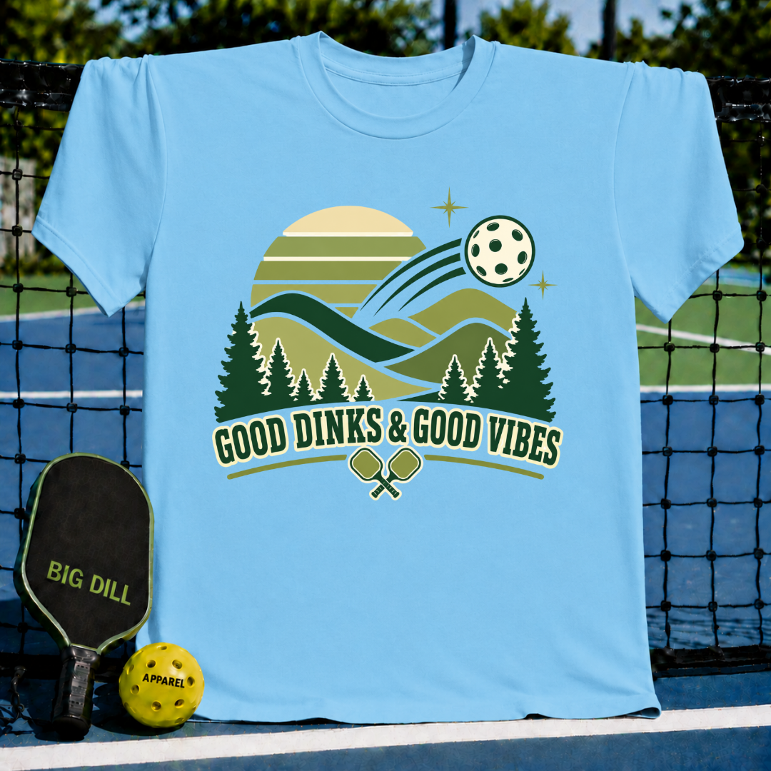 Light blue t-shirt featuring a retro pickleball graphic with mountains, trees, and the text Good Dinks & Good Vibes.