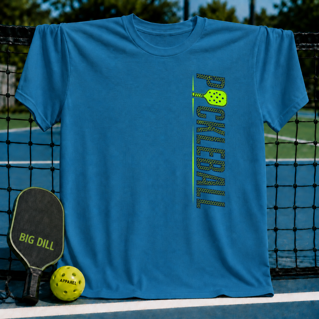 Blue unisex pickleball t-shirt with vertical green stacked text and paddle graphic, displayed on a court net.