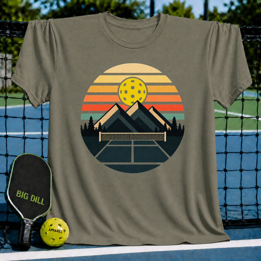 Olive green unisex t-shirt featuring a retro circular graphic of mountains, a pickleball net, and a sunset-colored sky.