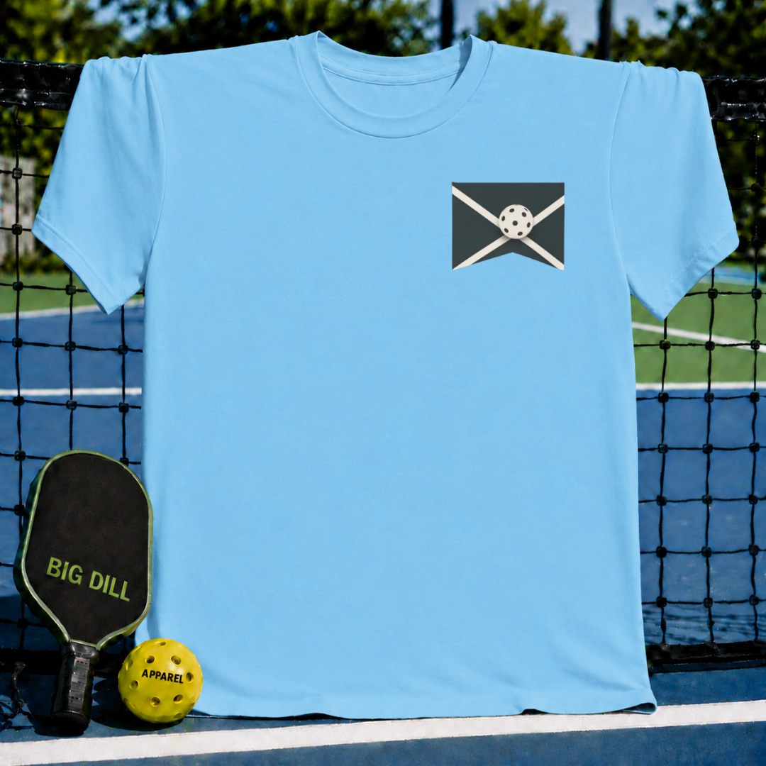 Light blue unisex crewneck T-shirt featuring a small chest graphic of a pickleball on a court line, displayed on a court.