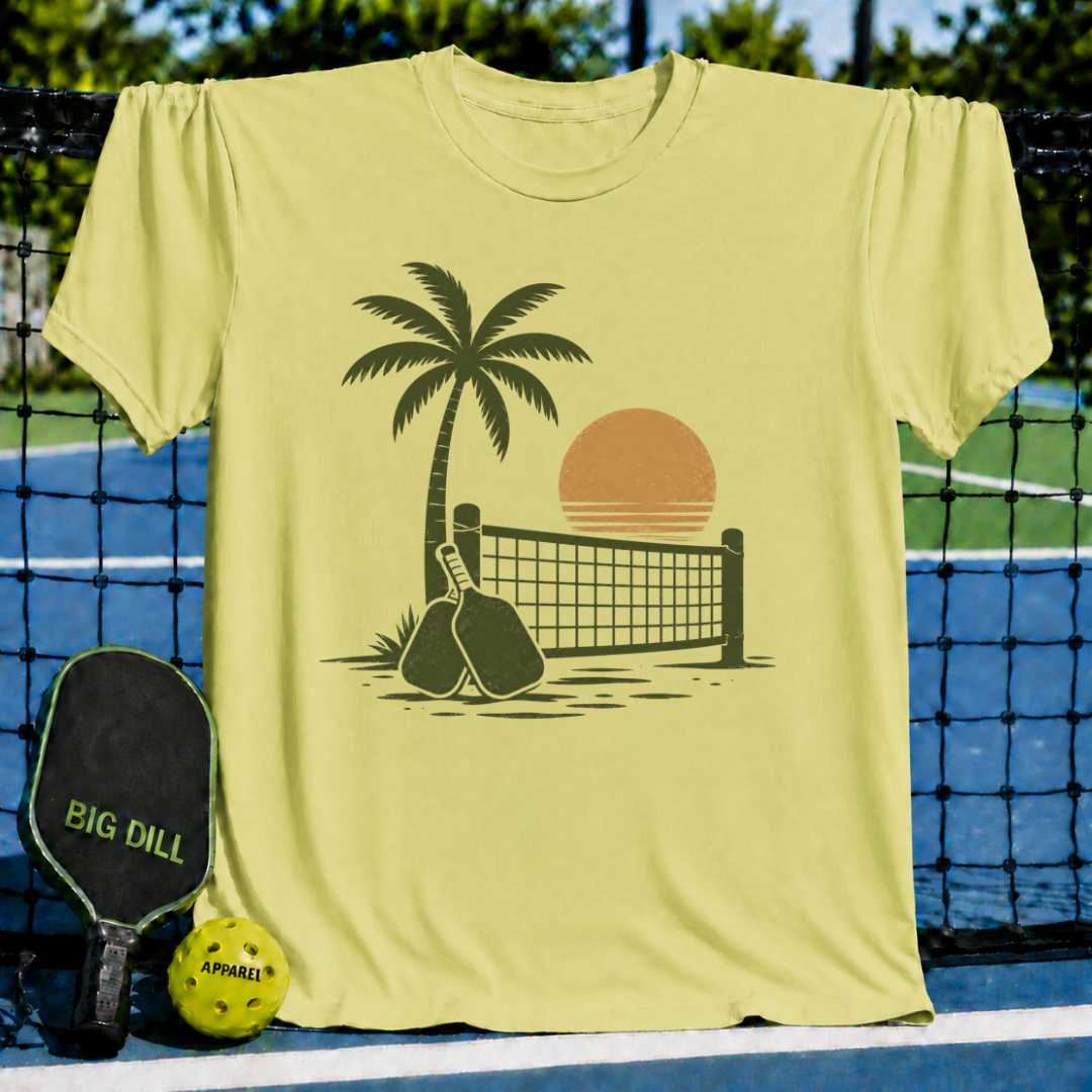 Butter yellow unisex t-shirt featuring a brown retro palm tree, pickleball net, and paddle graphic on a court background.