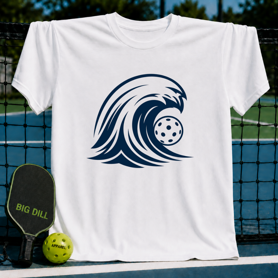 White unisex t-shirt featuring a navy blue cresting wave graphic with a pickleball, displayed on a pickleball court.