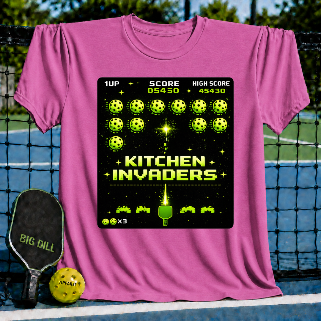 Pink unisex t-shirt featuring a retro pixel-art graphic of pickleballs attacking a paddle in a Space Invaders style.