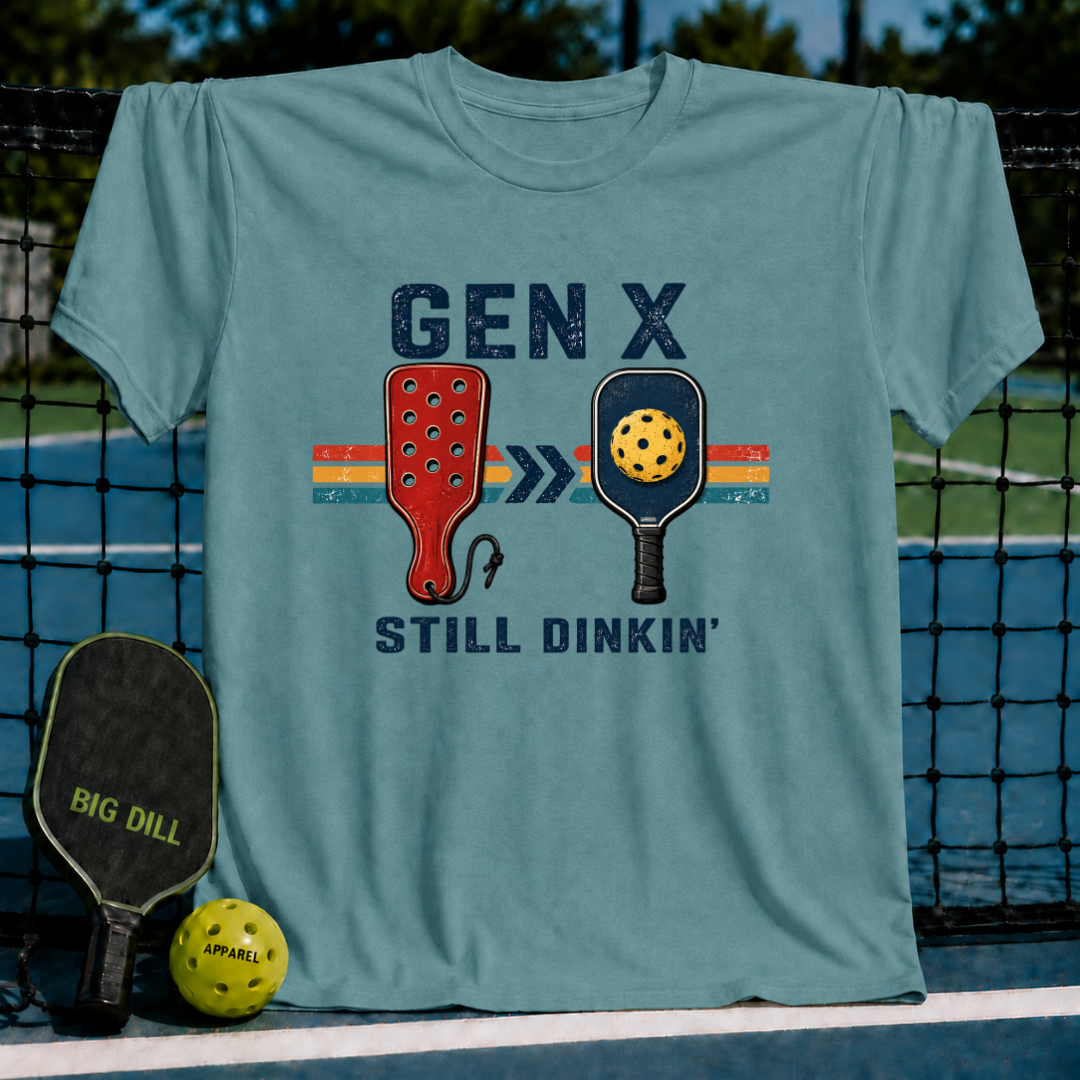 Blue-grey unisex t-shirt featuring a retro Gen X Still Dinkin' graphic with vintage paddles and a pickleball design.