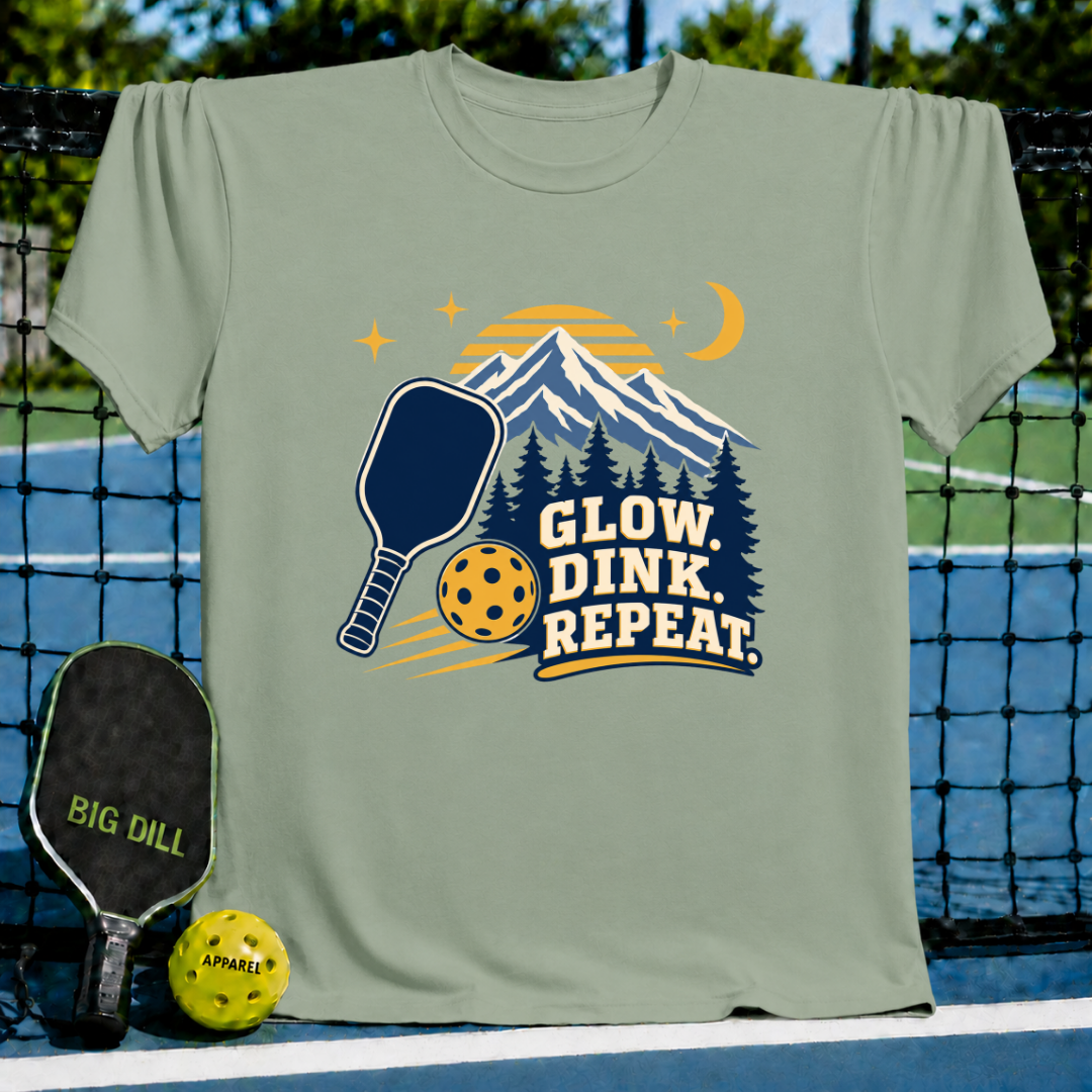 Sage green t-shirt featuring a mountain, pickleball paddle, and ball graphic with the text Glow, Dink, Repeat.